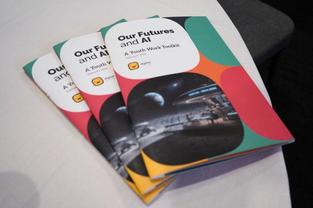 A stack of printed copies of the publication 'Our Futures and AI: A Youth Work Toolkit', arranged on a table.