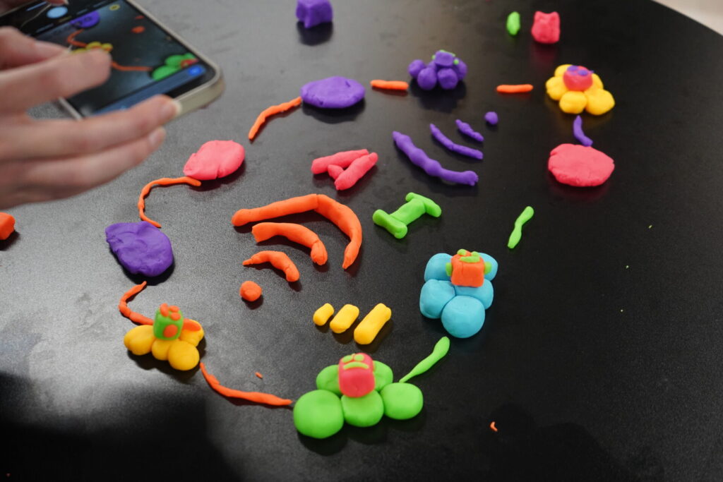 A colourful arrangement of playdoh shapes on a table, including WiFi symbols and the letters 'AI' inside a connected circuit of blobs and shapes.