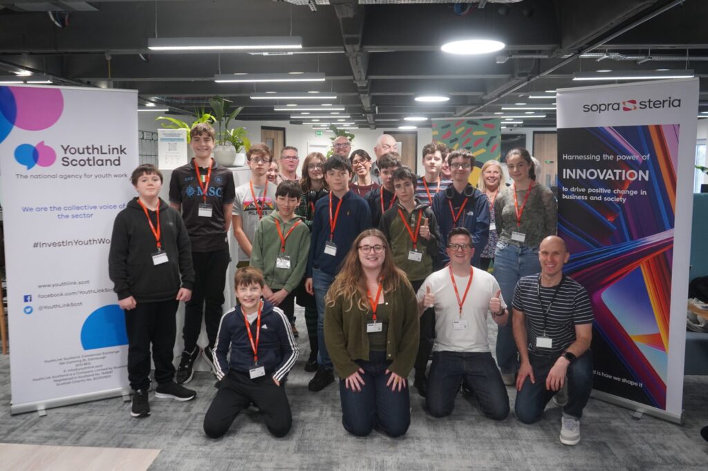 Group photo of youth workers, youth group members and Sopra Steria staff standing between banners for YouthLink Scotland and Sopra Steria.